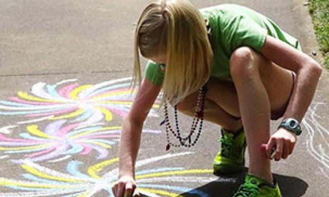 A young girl drawing with chalk on the pavement