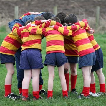 A group of boys huddled during a sporting match, wearing red and yellow striped gurnseys