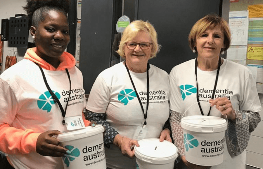 Three people wearing Dementia Australia t-shirts are holding cash collection buckets at a fundraising event.