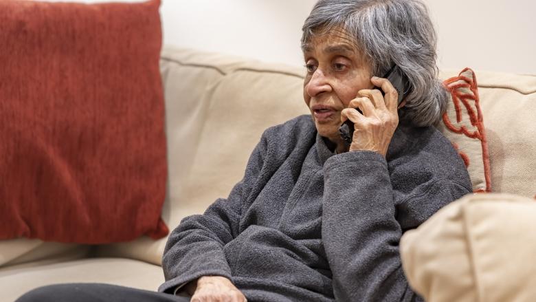 An elderly woman sitting on a couch whilst on the telephone.