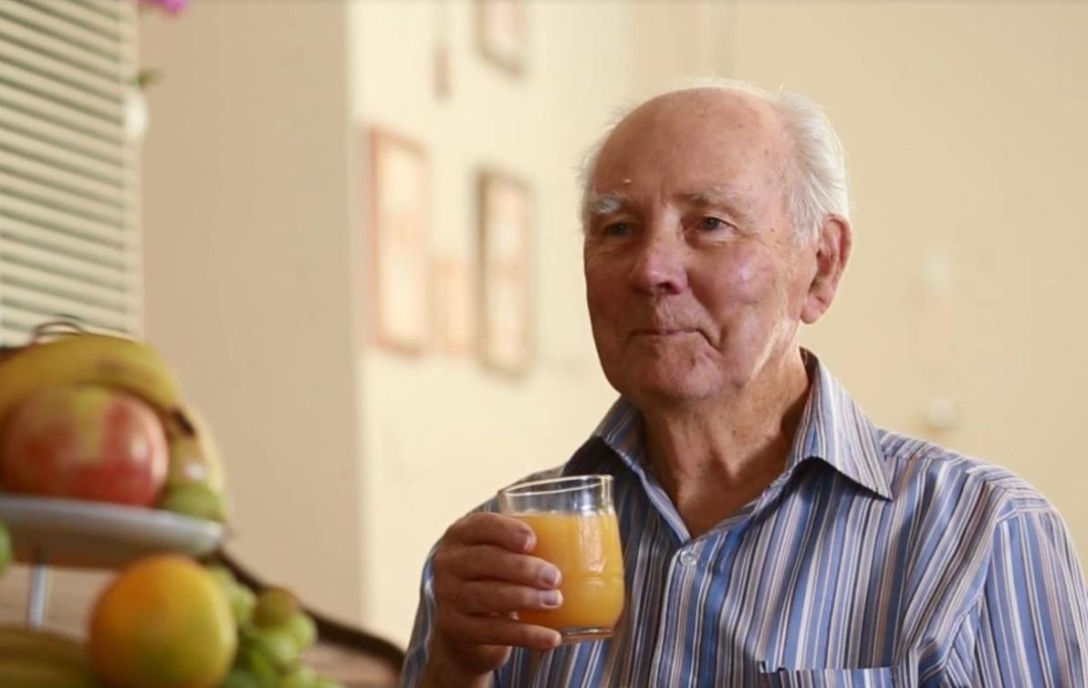 A man sitting at the breakfast table holding a glass of orange juice in his pyjamas