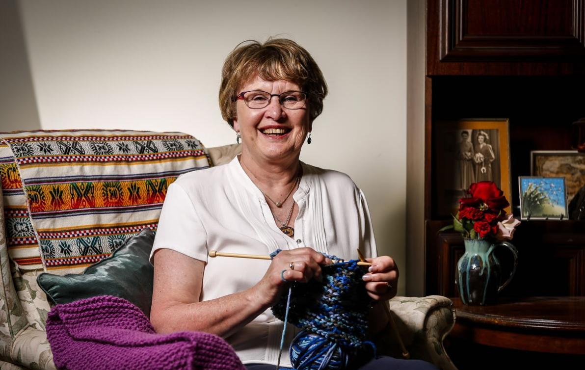 A smiling female sitting on her couch smiling whilst knitting