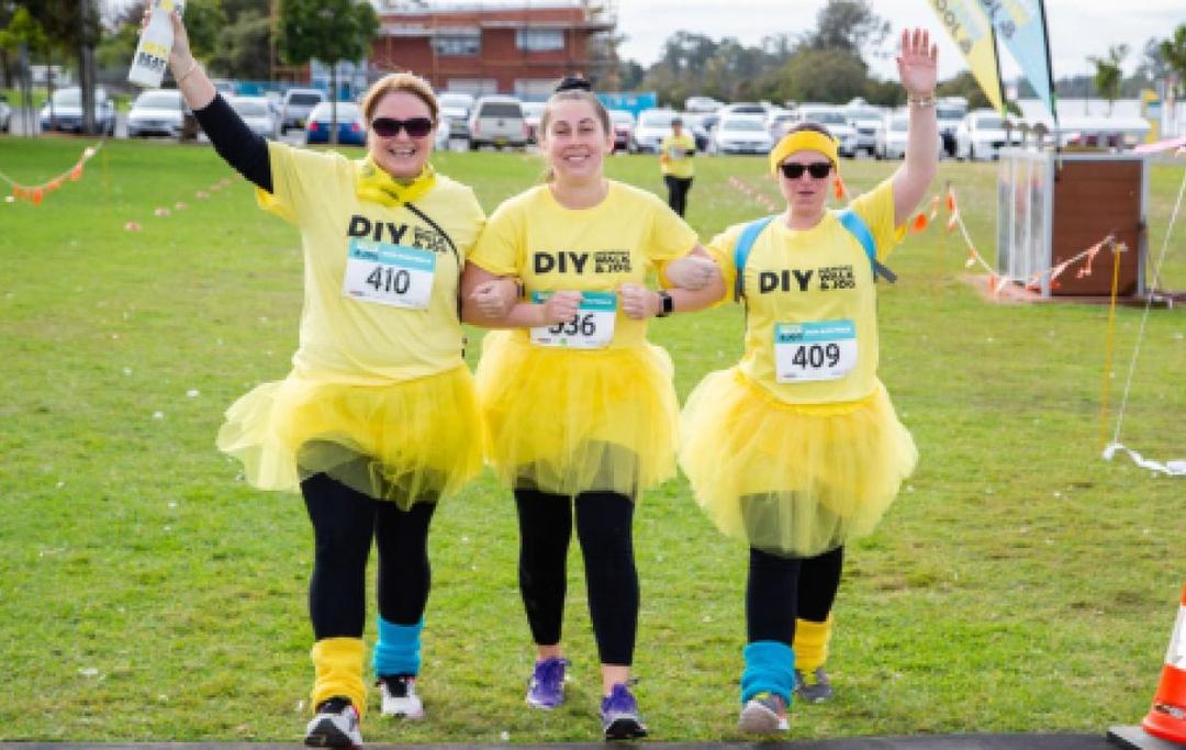 Three women in tutus stand at the finish line of a fun-run.