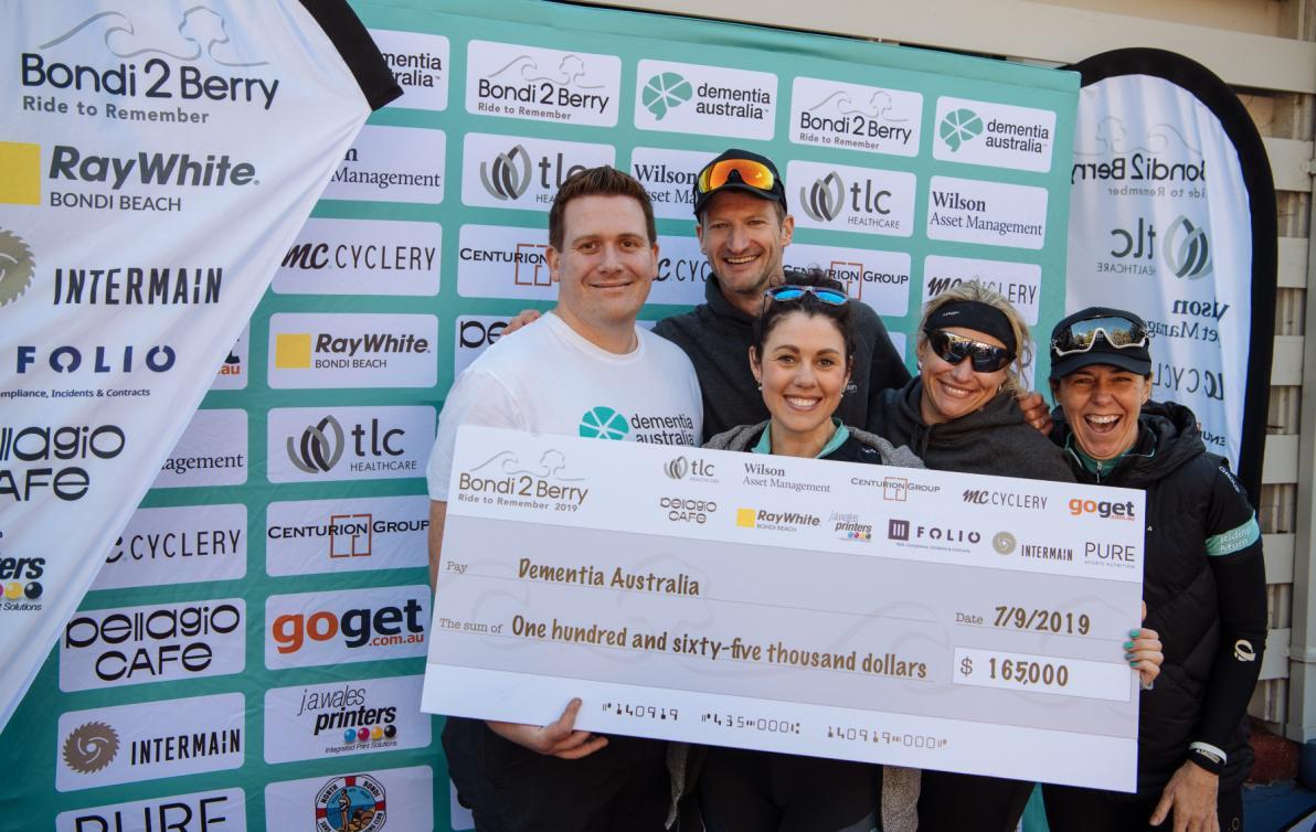 Five happy people in athletic wear stand in front of a giant novelty cheque.