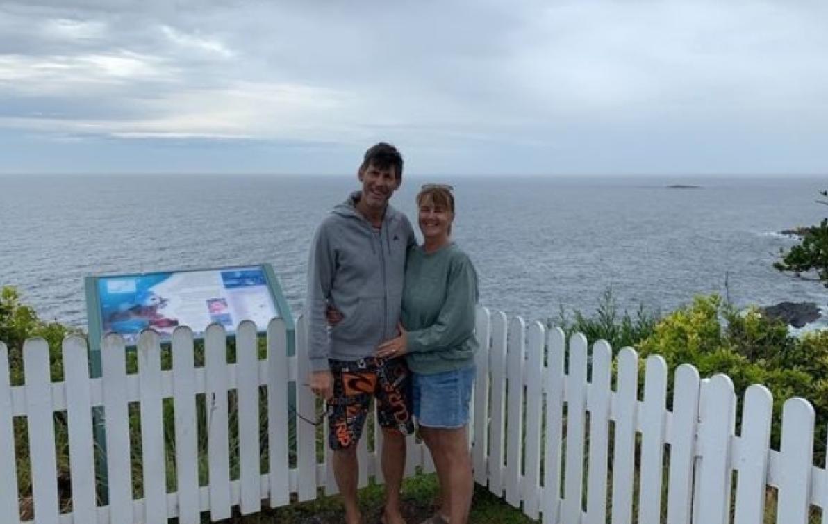 Alison and her husband Wayne posing in front of an ocean view.