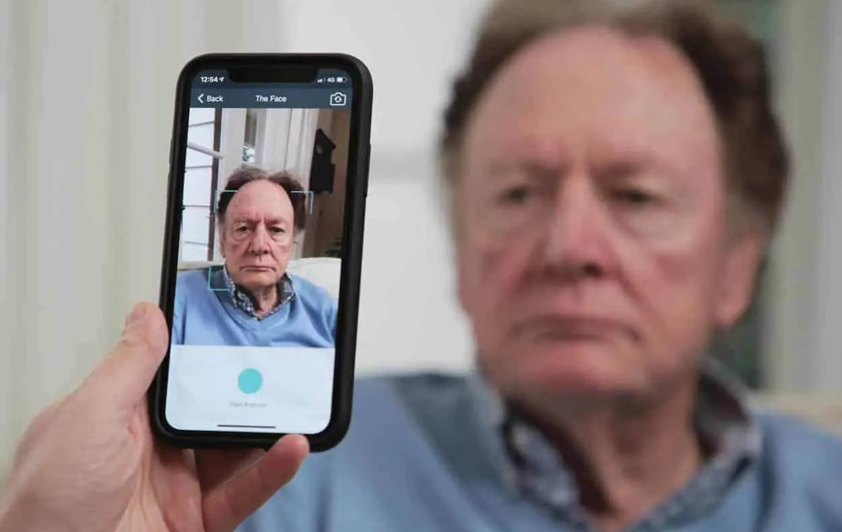 The PainChek app on a phone analyses the face of an older man