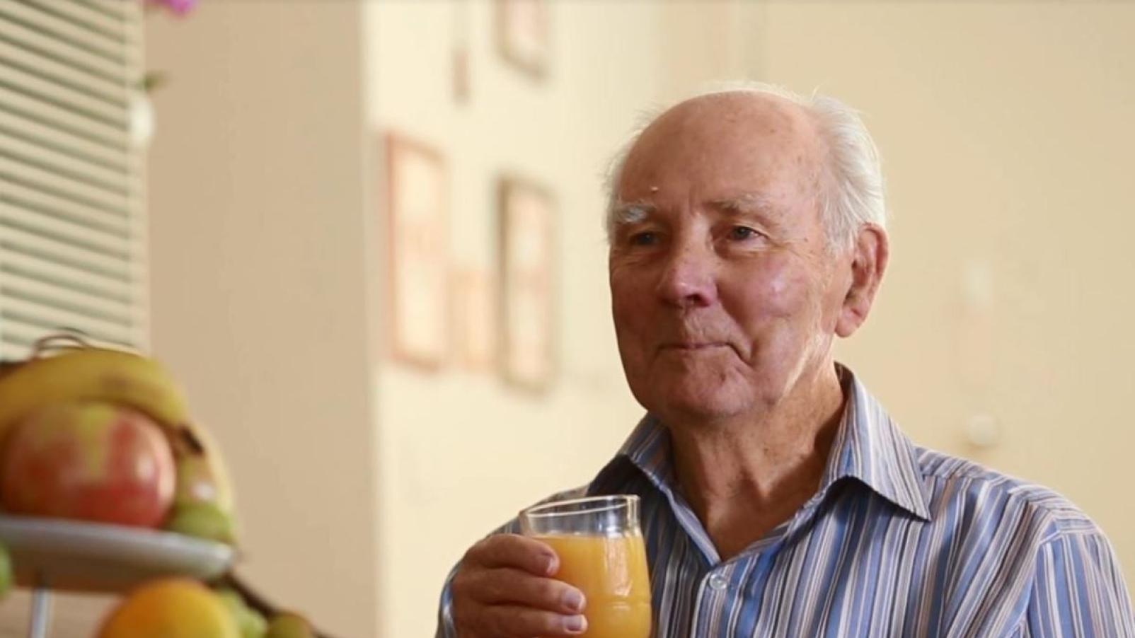 A man sitting at the breakfast table holding a glass of orange juice in his pyjamas