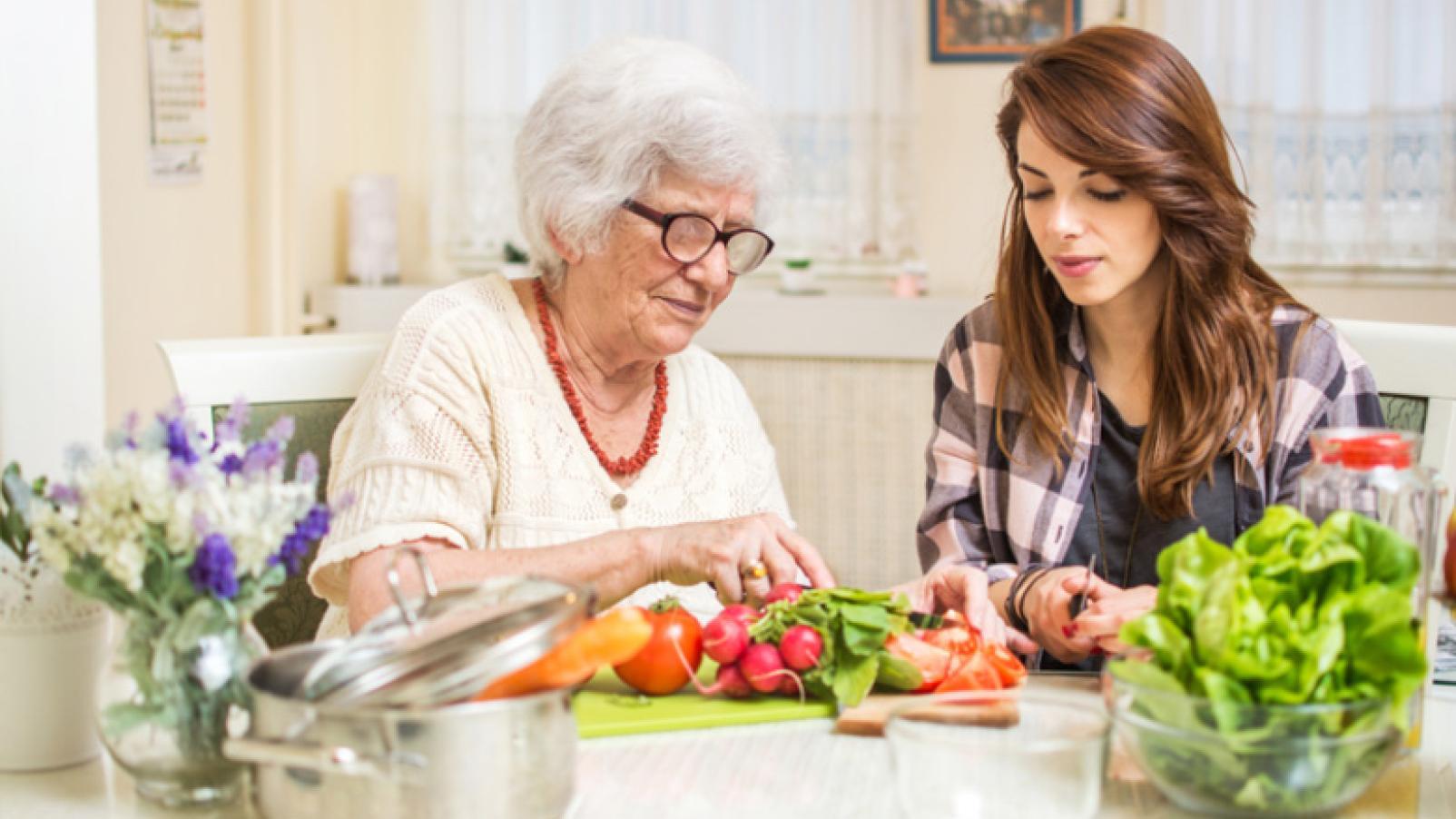 An elderly woman and a younger lady in a kitchen with vegetables