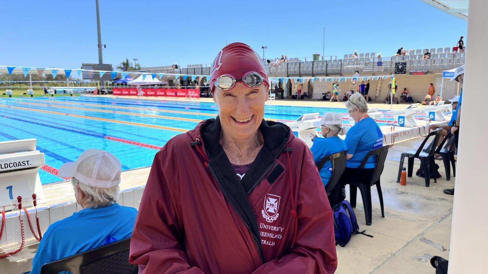 Dementia Advocate Andree Ernst in a University of Queensland jacket and a swimming cap and goggles, beside a swimming pool.