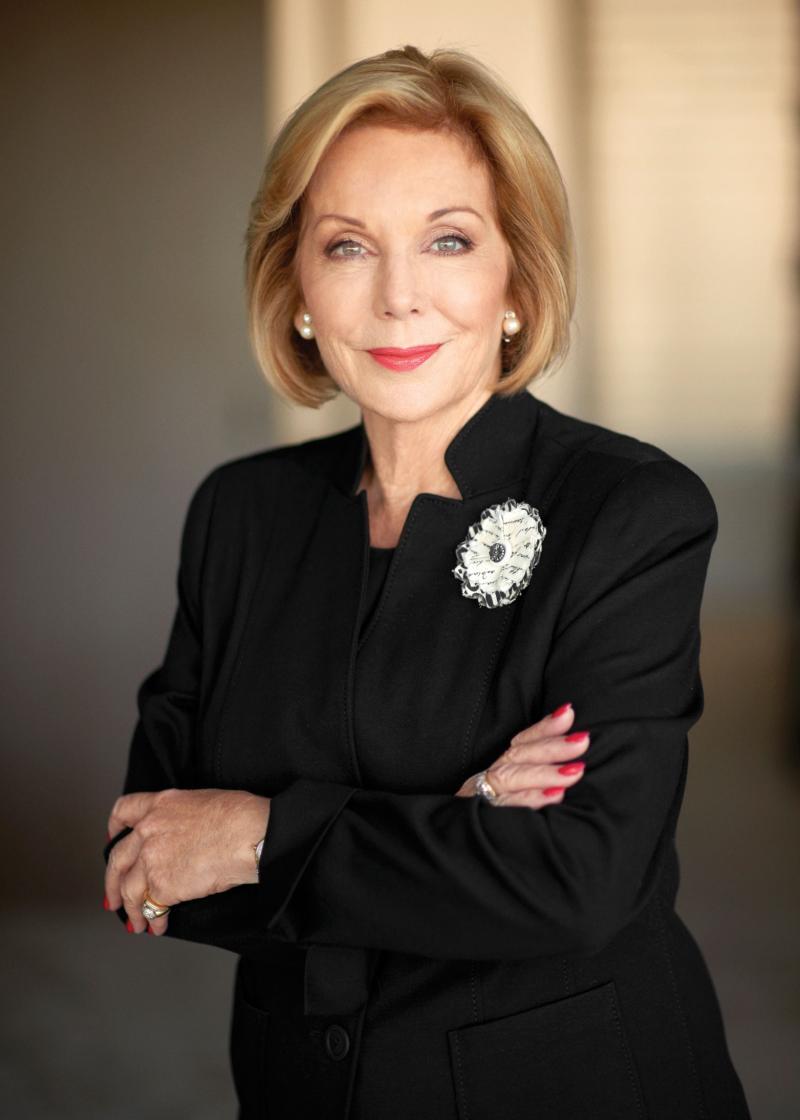 Ita Buttrose portrait wearing black clothing, smiling at the camera with arms crossed