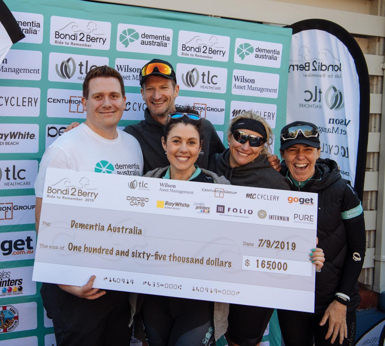 Five happy people in athletic wear stand in front of a giant novelty cheque.