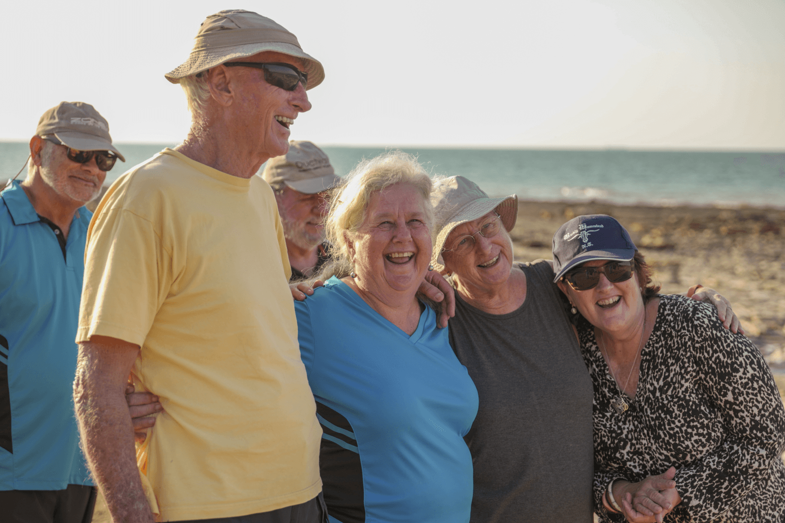 Some people standing at a beach with arms around each other smiling