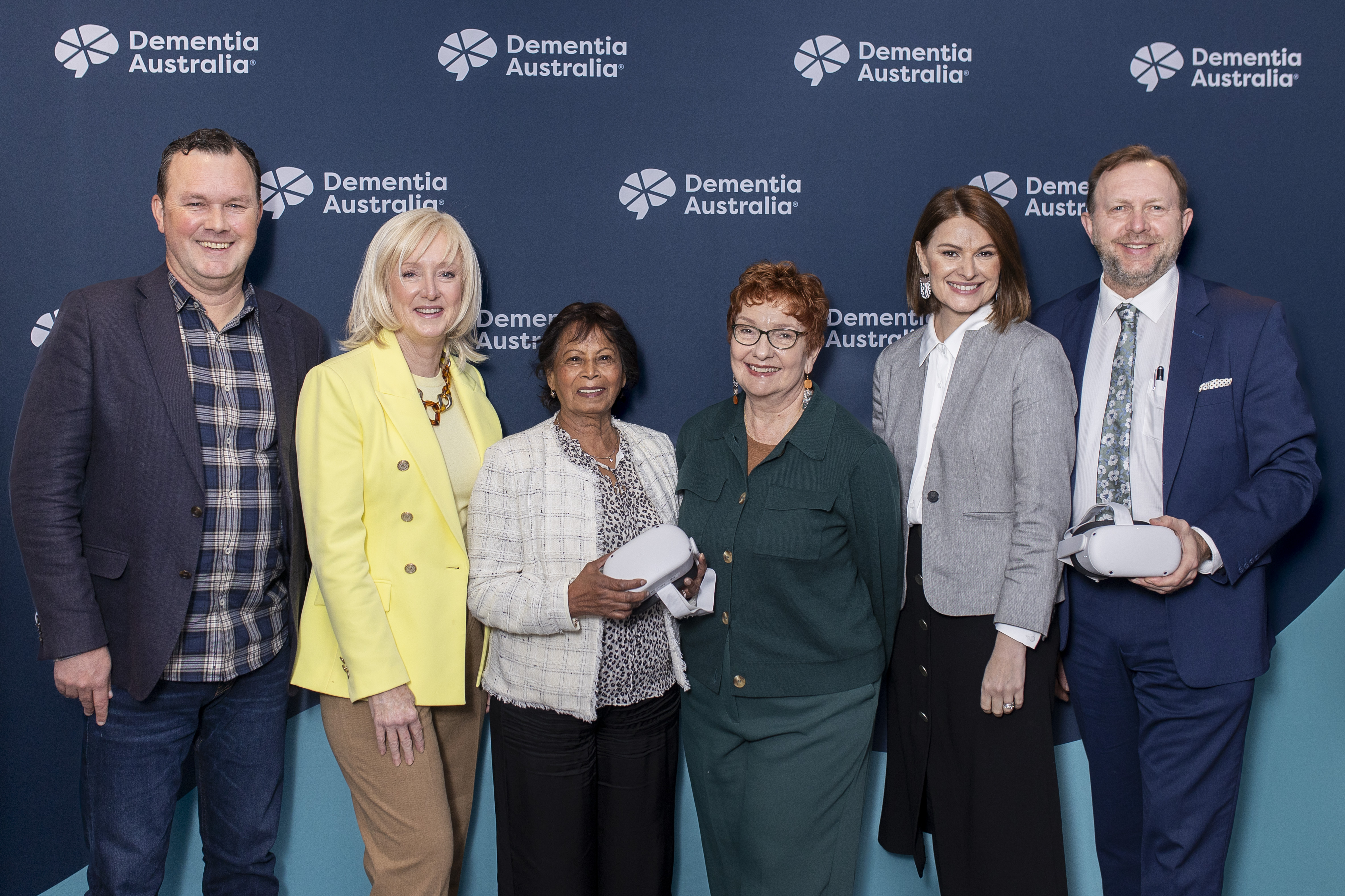 A group of people stand in front of a Dementia Australia banner smiling