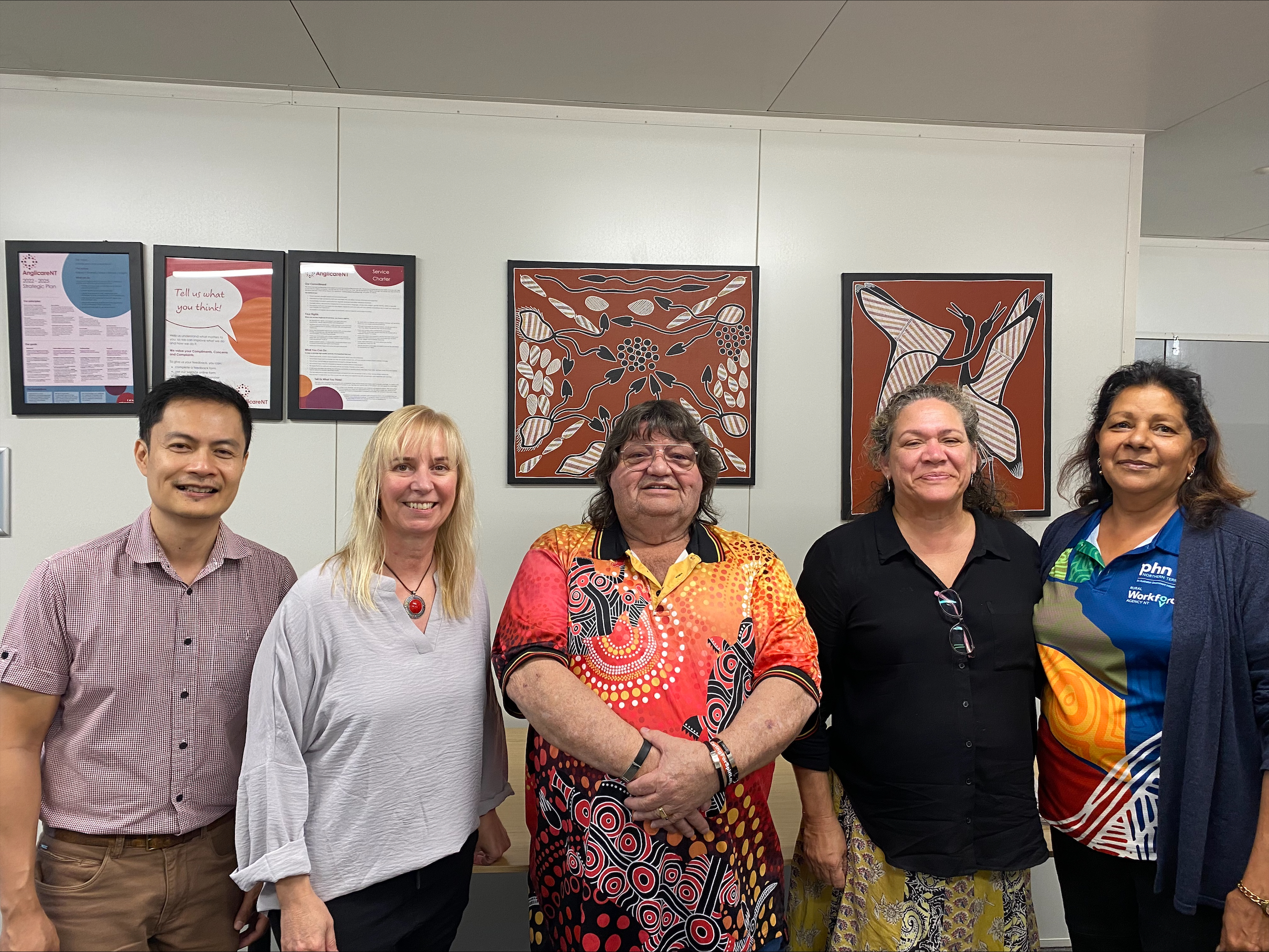 A group of people stand together in front of Aboriginal artwork